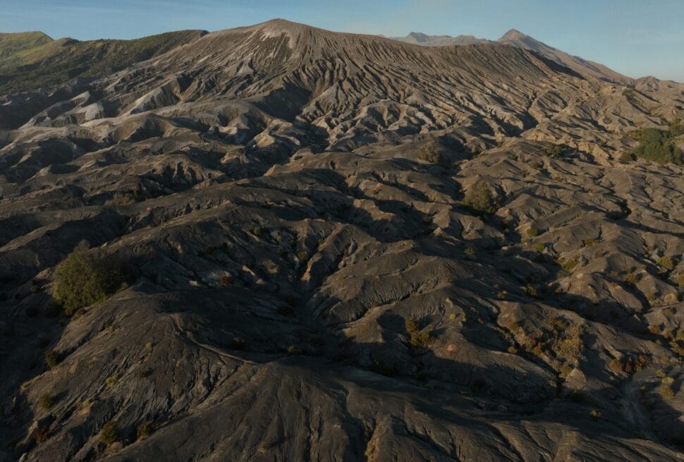 Wide aerial view of Indonesia's Pasir Berbisik, a vast volcanic sand sea with eroded hills and distant mountains.