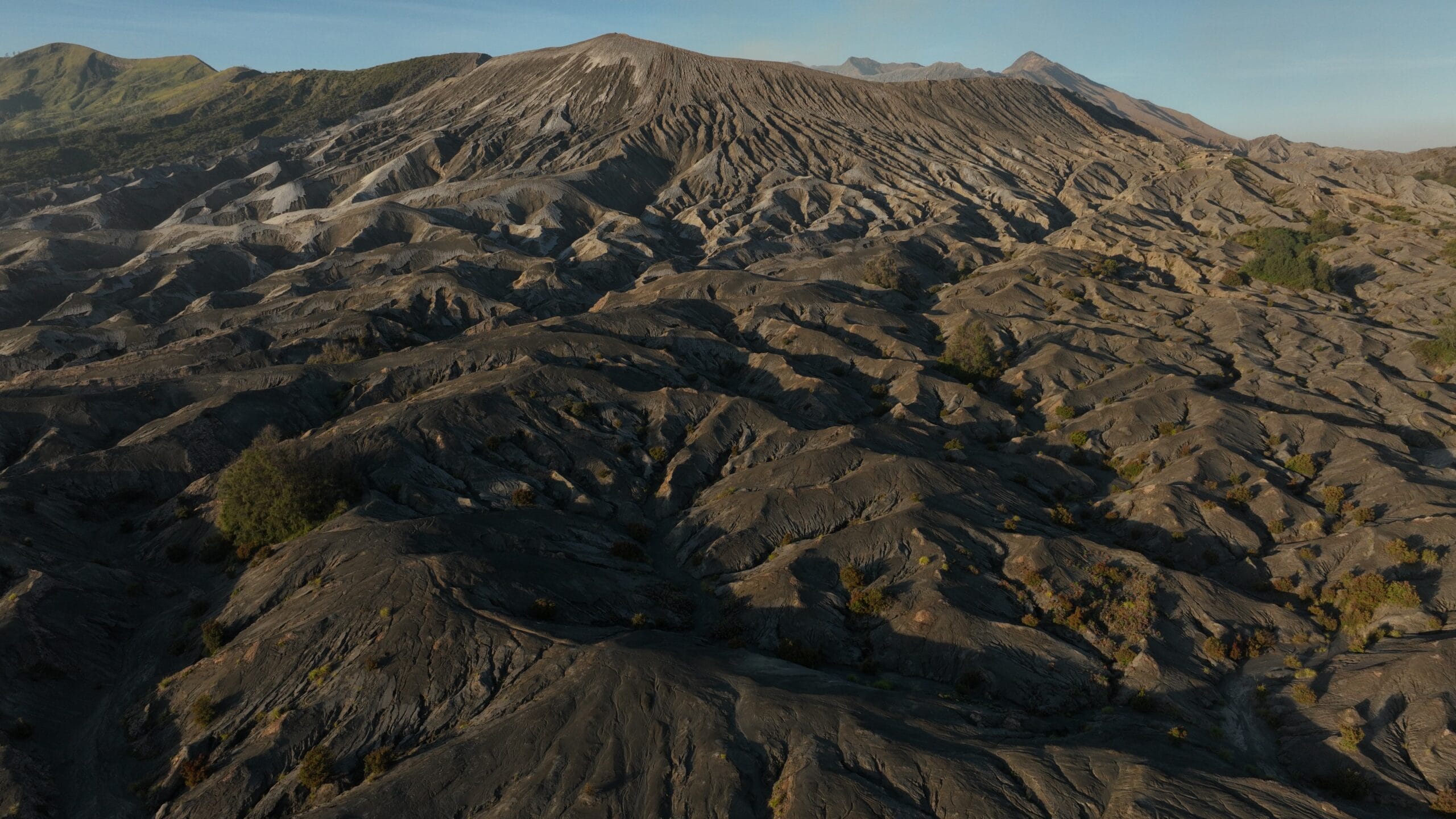 Wide aerial view of Indonesia's Pasir Berbisik, a vast volcanic sand sea with eroded hills and distant mountains.