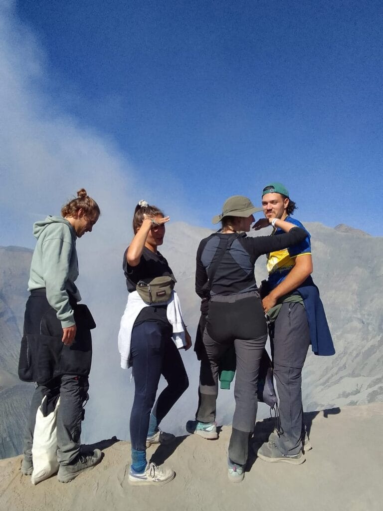 Four hikers gaze at the steaming crater of Mount Bromo volcano in Indonesia, enjoying the epic view