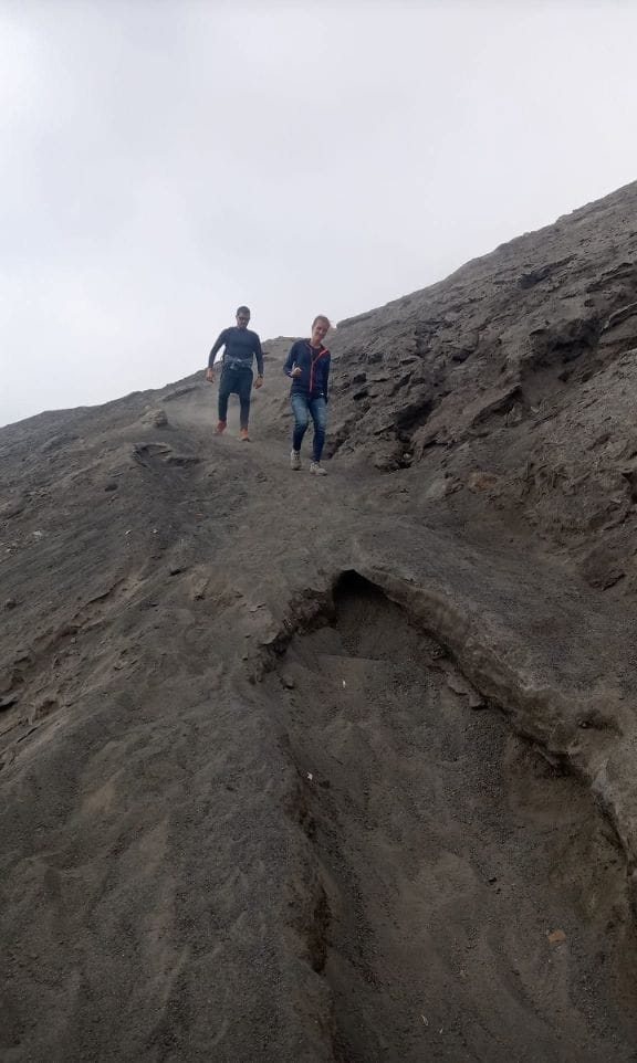 Two hikers carefully descend a steep, dusty volcanic path on Mount Bromo, showcasing challenging terrain.