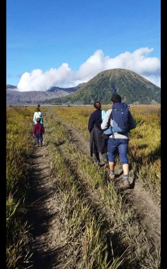 Family hiking on Dalan Jaran (horse route) with Gunung Batok and active Bromo volcano in background, East Java, Indonesia