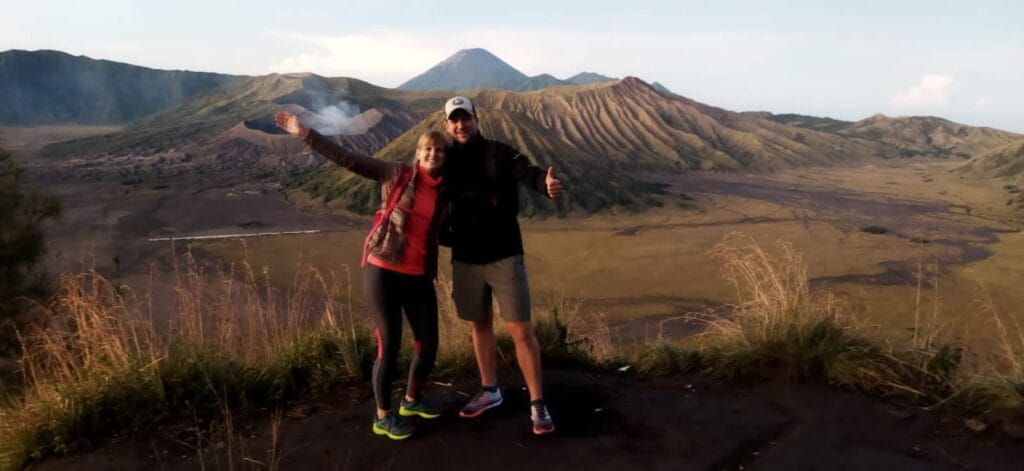 Couple posing at King Kong Hill with Mount Bromo active volcano and Mount Batok in the vast caldera, Indonesia.