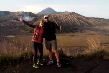 Couple posing at King Kong Hill with Mount Bromo active volcano and Mount Batok in the vast caldera, Indonesia.