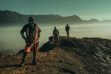 Hikers at Gunung Kursi enjoying a hidden sunrise spot above a sea of clouds, mountains in background.