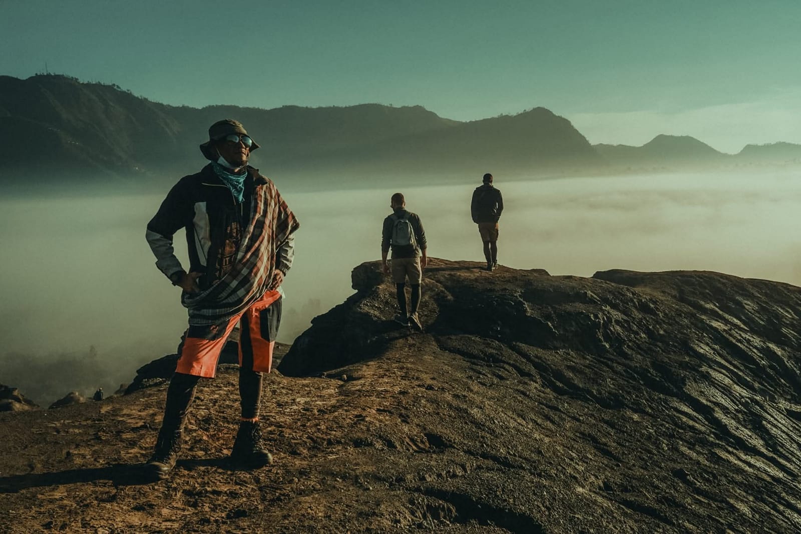 Hikers at Gunung Kursi enjoying a hidden sunrise spot above a sea of clouds, mountains in background.