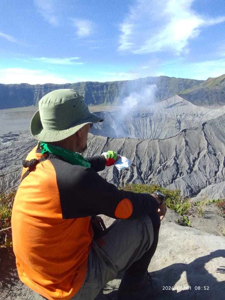 Hiker on Mount Batok overlooks active Mount Bromo volcano crater with smoke in East Java, Indonesia
