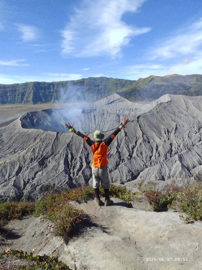 Hiker with arms outstretched admiring Mount Bromo volcano from Gunung Batok summit, Indonesia.