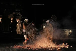 High-energy action shot of a dancer kicking burning coconut husks during the Sanghyang Jaran Bali traditional dance.