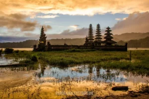 A multi-tiered traditional Balinese temple standing gracefully in a lake, reflecting perfectly in the water during a golden sunset.