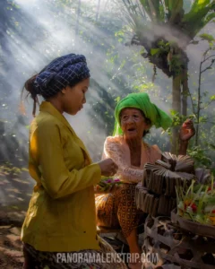 An elderly Balinese woman and a young woman in traditional dress preparing daily floral offerings in a misty, sunlit garden during a Bali culture tour.