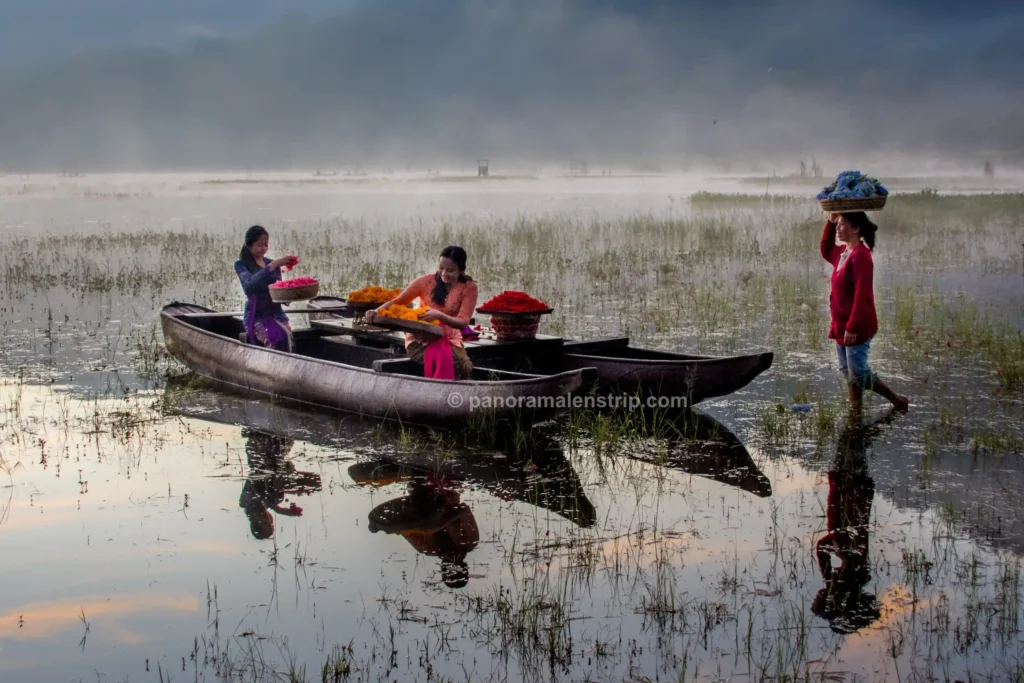 Three local women preparing vibrant floral offerings on a traditional canoe in a misty lake.