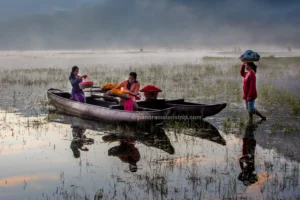 Three local women preparing vibrant floral offerings on a traditional canoe in a misty lake.