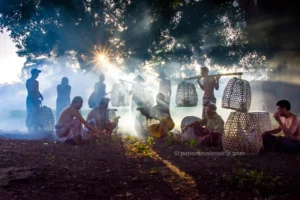 Men gathering with rooster cages in the morning mist at a Bali traditional village.