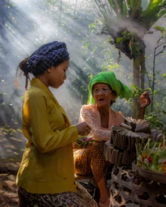 Two Balinese women preparing colorful canang sari offerings in the morning sunlight during a Bali culture tour.