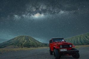 Red jeep at Bukit Widodaren Bromo with Mount Batok and Mount Widodaren under the Milky Way night sky
