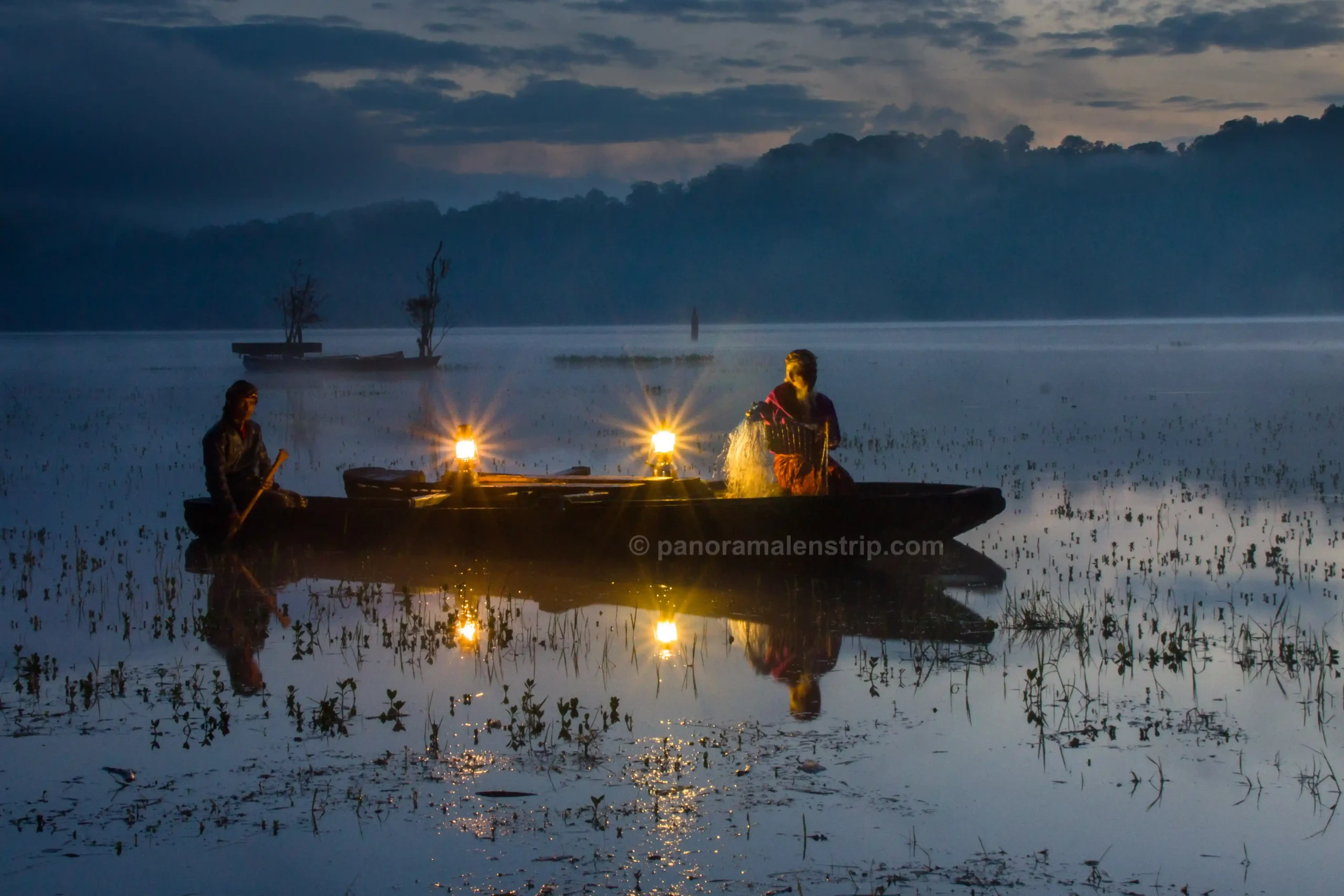 Two locals on a traditional canoe illuminated by glowing lanterns before dawn, showcasing the quiet essence of Bali spiritual healing.