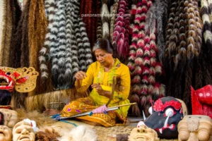 A Balinese woman in a yellow kebaya weaving coarse fibers for a traditional Barong costume inside a vibrant Bali artisan village.