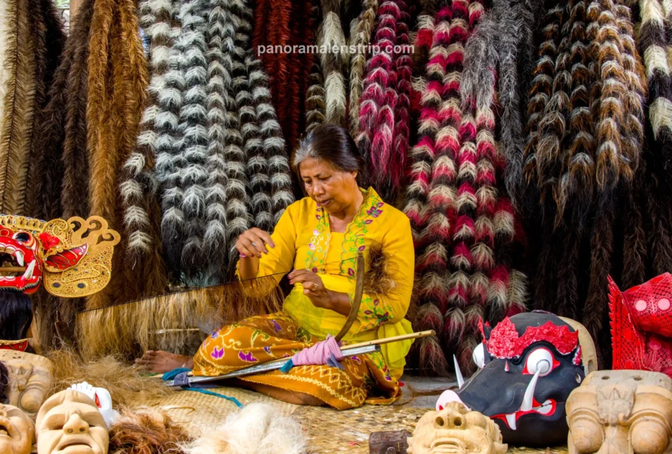 A Balinese woman in a yellow kebaya weaving coarse fibers for a traditional Barong costume inside a vibrant Bali artisan village.