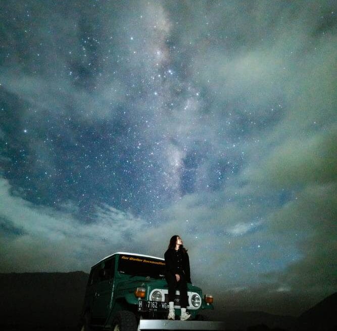A woman posing on a jeep under a misty Milky Way sky at Pasir Berbisik in May