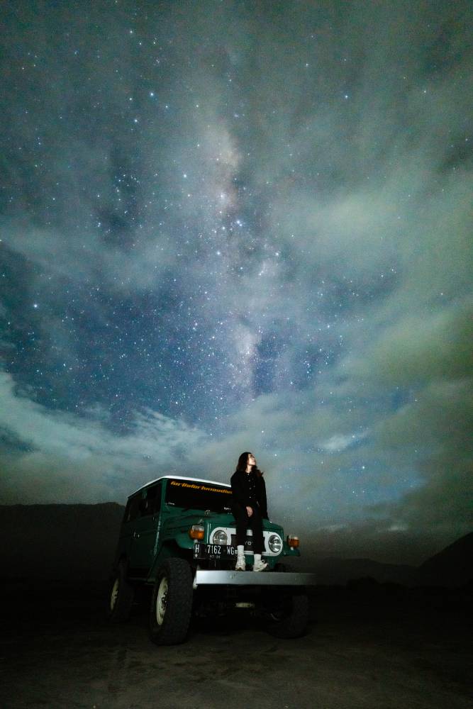 A woman posing on a jeep under a misty Milky Way sky at Pasir Berbisik in May