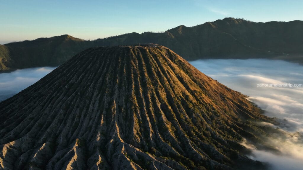 Golden sunrise light illuminating the ridges of Mount Batok, rising majestically above a thick sea of white clouds in the Tengger caldera.