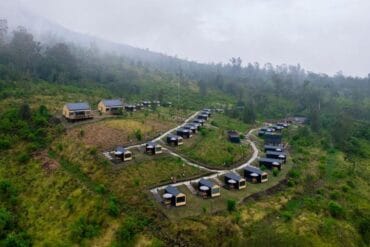 Aerial drone view of Bobo Cabin Hotel in Paltuding surrounded by lush green hills and misty mountain scenery.