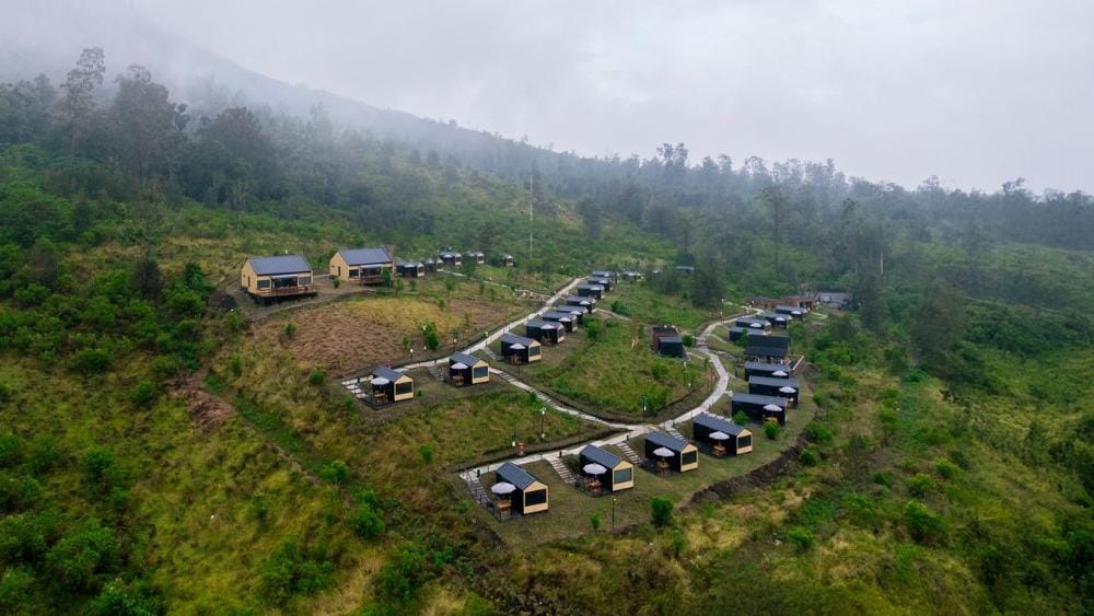 Aerial drone view of Bobo Cabin Hotel in Paltuding surrounded by lush green hills and misty mountain scenery.