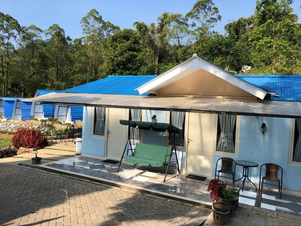 Exterior view of a Bromo Camp House room and courtyard in Desa Sapikerep, featuring a blue-roofed cabin with a shaded porch and seating area.