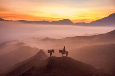 Horse and basket carrier silhouetted against a sunrise over Mount Bromo, Indonesia.