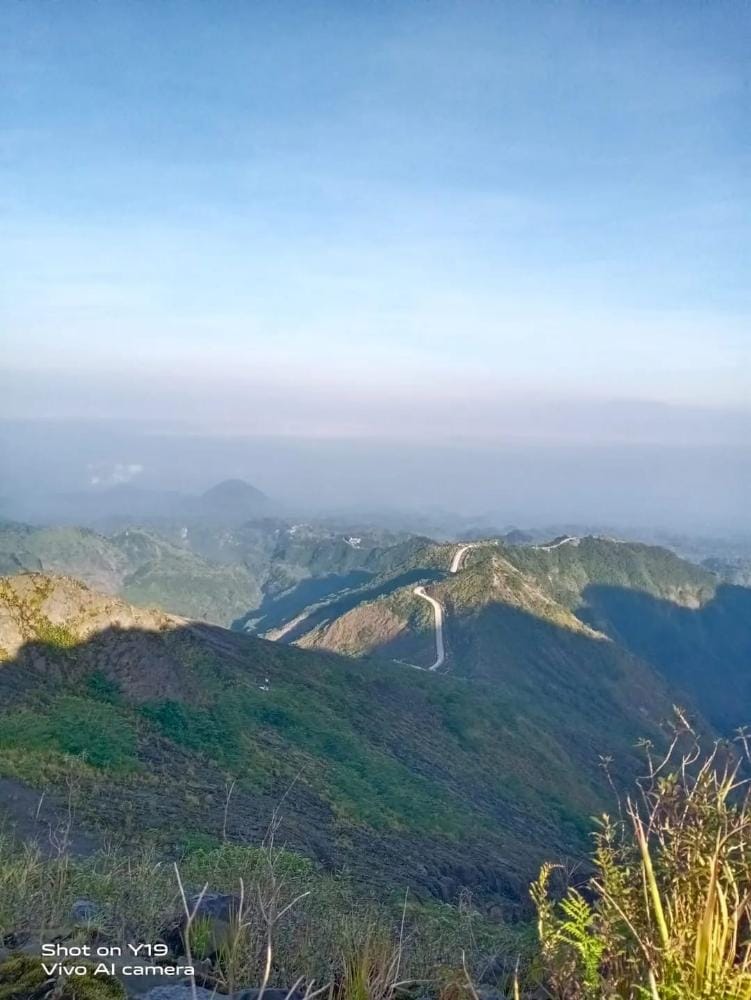 Panoramic view of Ojek Kelud Road from the summit of Mount Welirang near Mount Kelud, with winding mountain roads and lush green volcanic slopes.