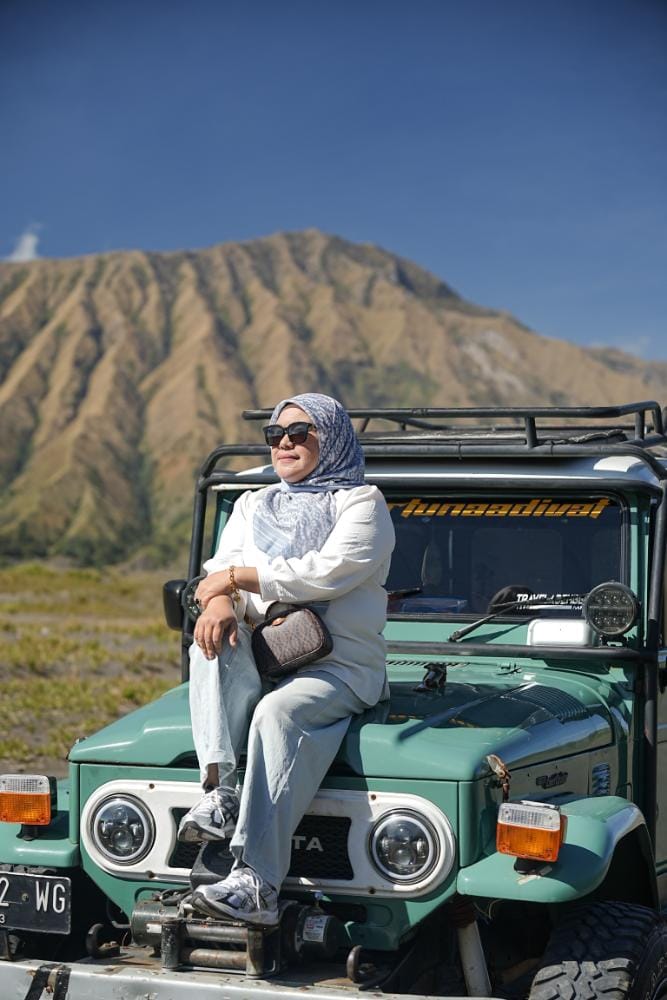 A woman sitting on top of a jeep with Mount Bromo in the background at Bukit Widodaren.