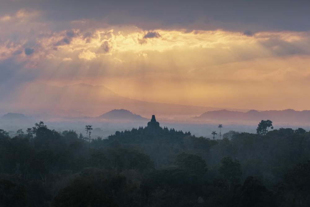 Sunrise over Borobudur Temple viewed from Puthuk Situmbu, with misty hills and golden light