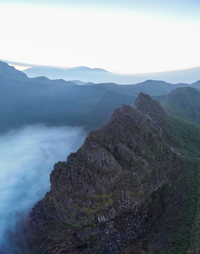 Sunrise over the rugged peak of Tebing Lembu Suro at Gunung Kelud, with dramatic mountains and mist below.