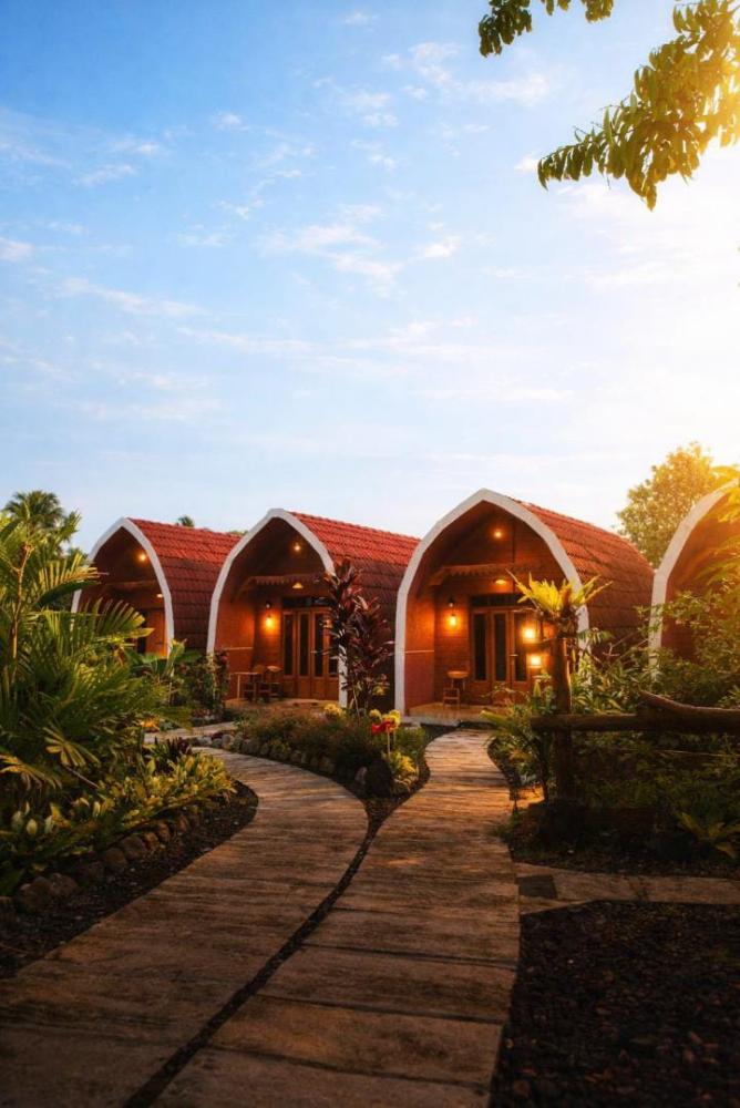 Cottages at Indah Damai Cottage glowing softly before sunrise, with a curved wooden pathway and tropical garden.