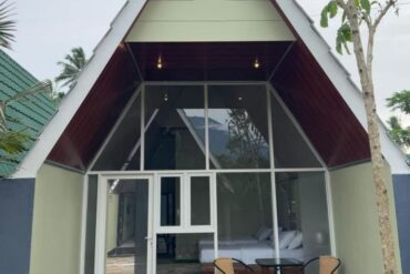 A modern A-frame cottage room in Kaliningrad with a glass front, patio seating, and a hill in the background.