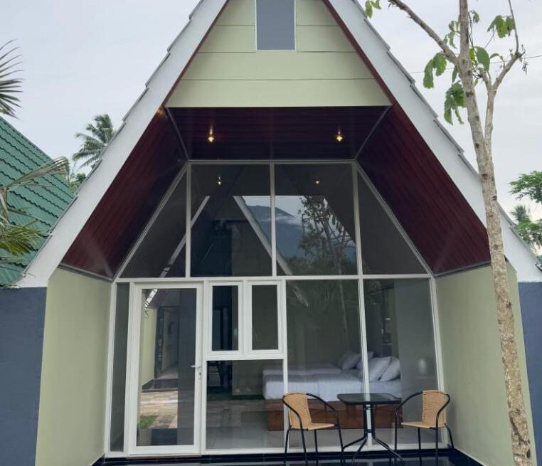 A modern A-frame cottage room in Kaliningrad with a glass front, patio seating, and a hill in the background.