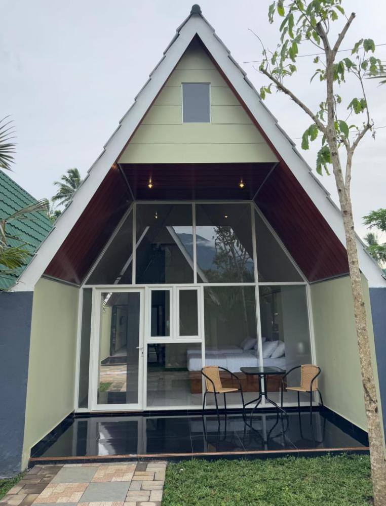 A modern A-frame cottage room in Kaliningrad with a glass front, patio seating, and a hill in the background.
