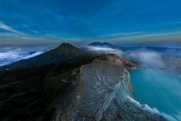 Drone view of sunrise at the entrance to Kawah Ijen, with the crater rim, turquoise lake, and clouds above the volcano