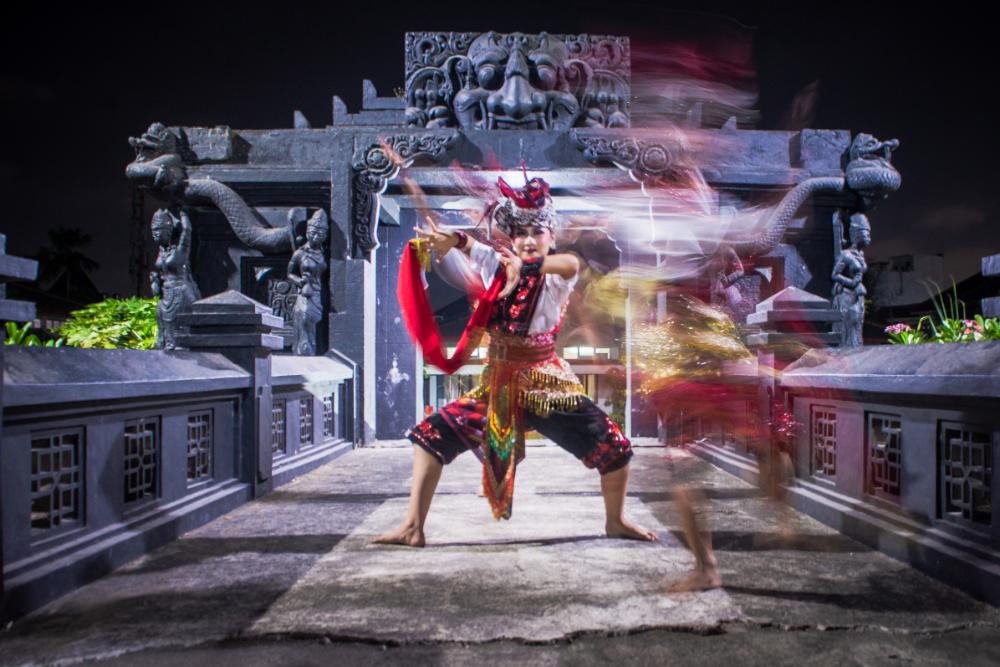 Traditional Tari Topeng dancer performing in front of an ornate stone gateway in Malang, Indonesia