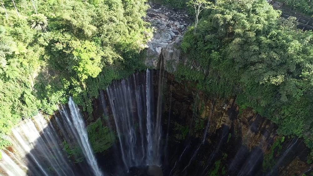 Aerial drone view of Tumpak Sewu Waterfall surrounded by lush green cliffs in East Java, Indonesia.